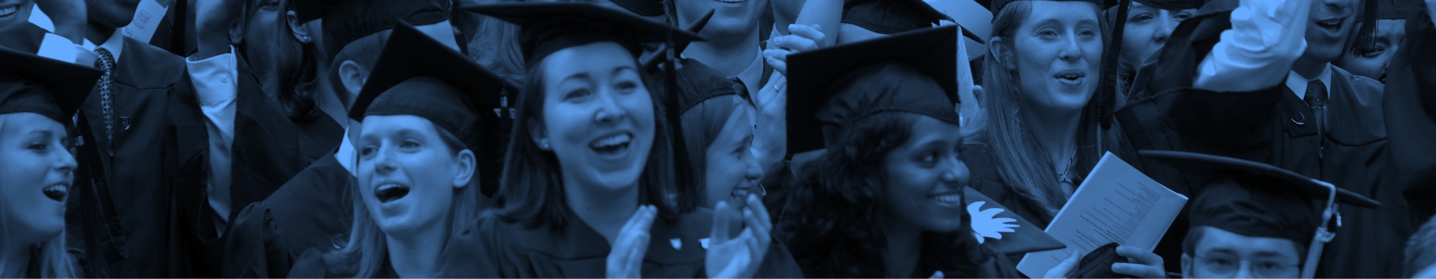 A crowd of graduates cheering and smiling during commencement